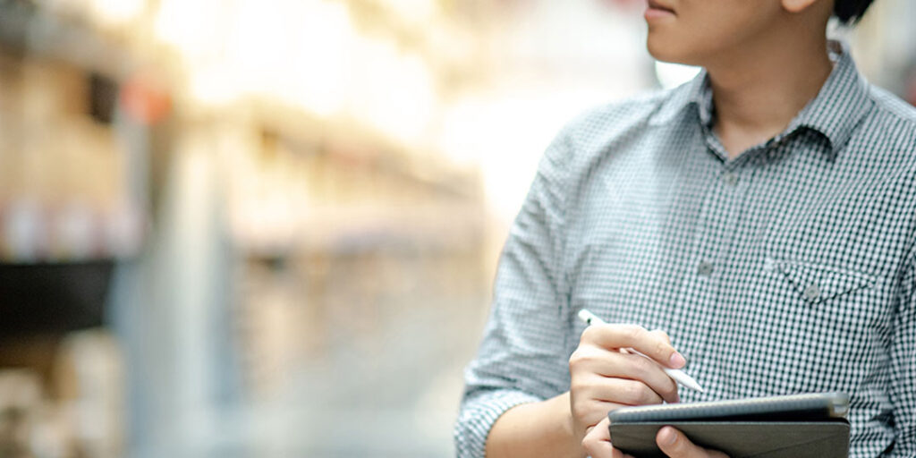 Person working in a warehouse holding a tablet and using a stylus.