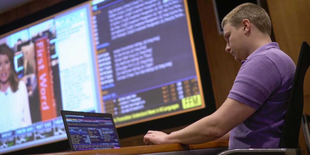 Young male student working on a computer with a large screen in the background.