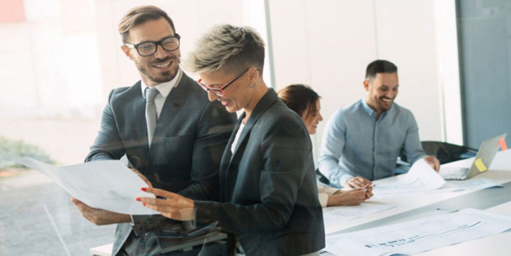 Woman standing confidently next to her male counterpart reviewing a supply chain plan.