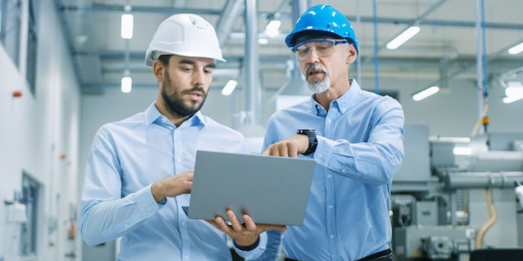 Head of the project holds laptop and discusses product details with chief engineer while they walk through modern factory.