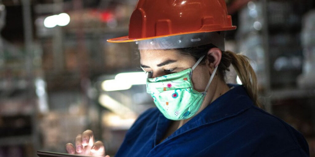 A person, using a mask and industry gear while looking at a mobile device