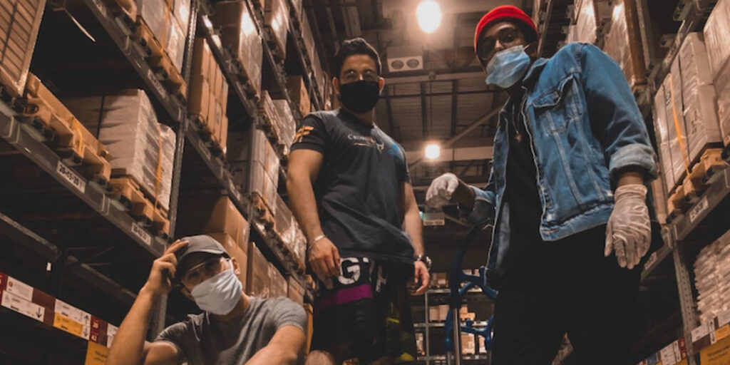 A group of men in warehouse. All three men are wearing masks.