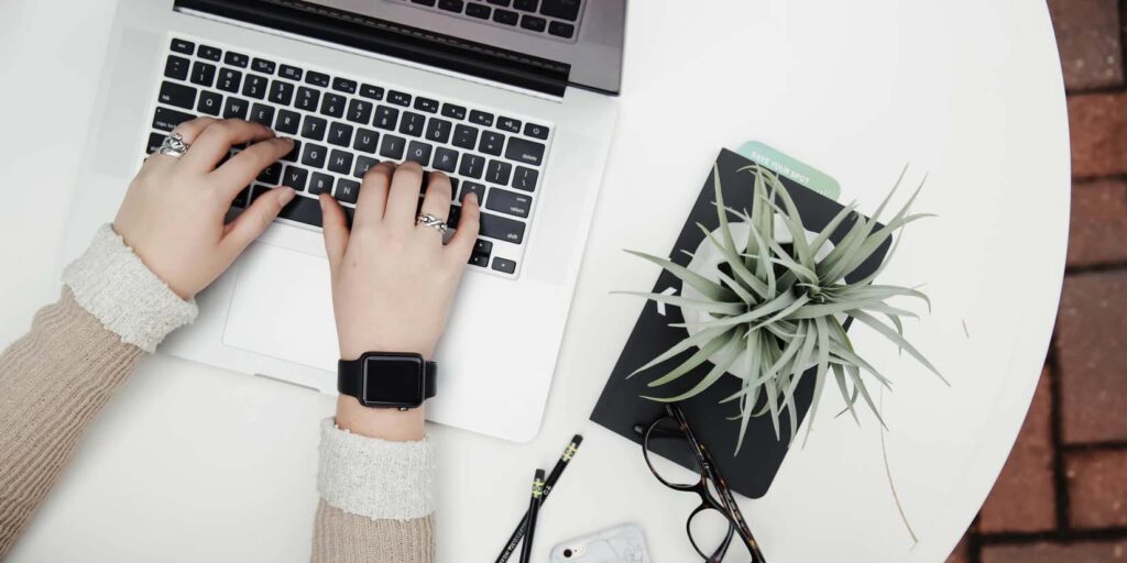 Woman typing on a laptop that is set on a clean white desk.