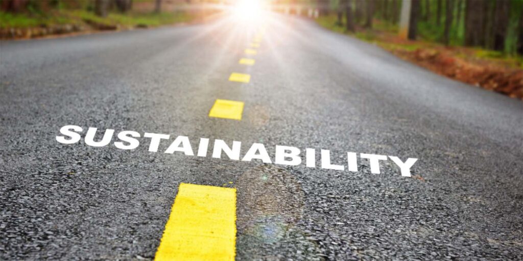 A paved road with the sun in the distance with the word "Sustainability" in the foreground.